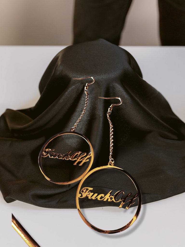 Gold Hoop Earrings on a chain with the words Fuck Off written in cursive on a black satin background.